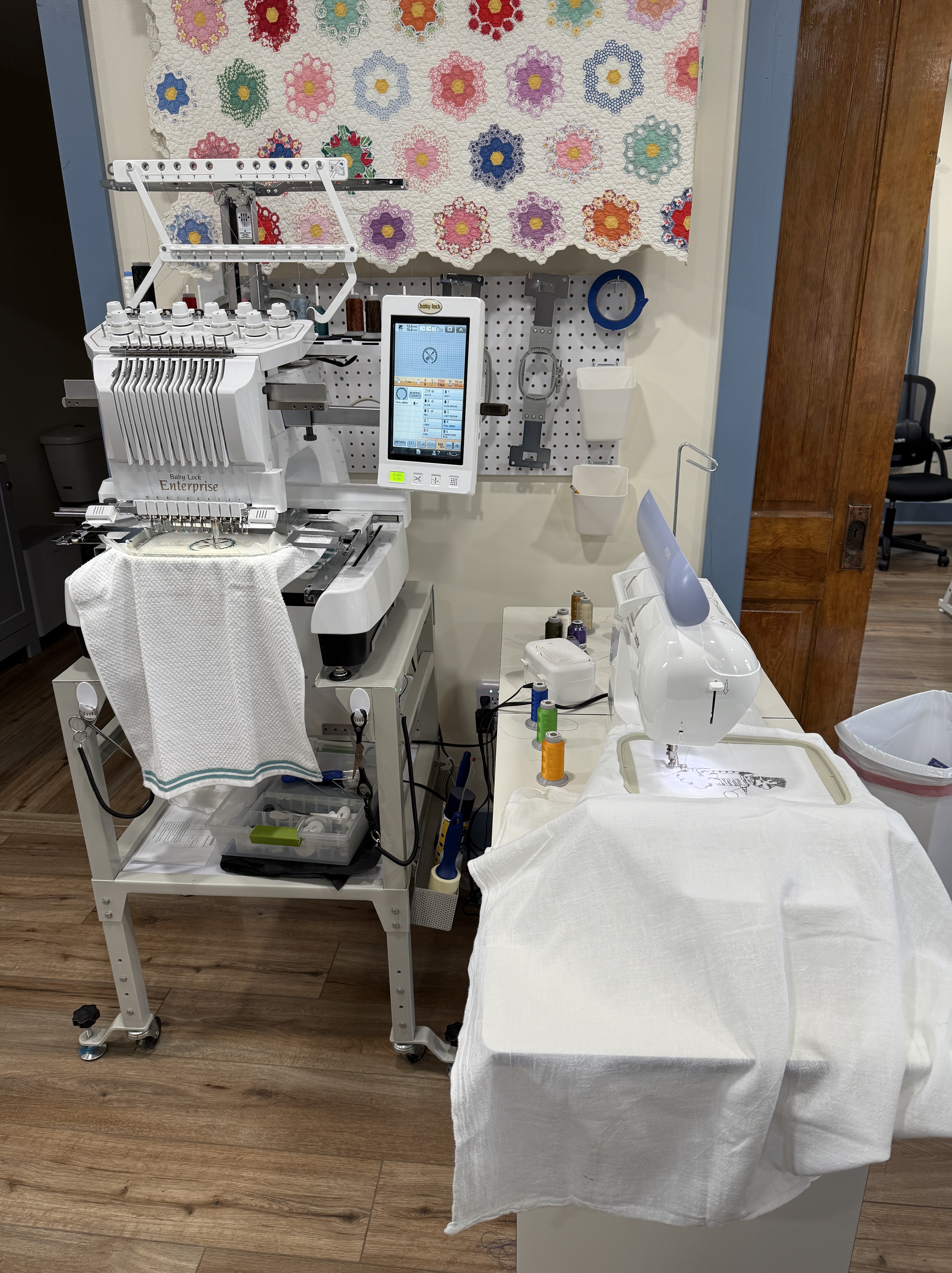 A ten needle embroidery machine and a single needle machine are both stitching designs on towels.